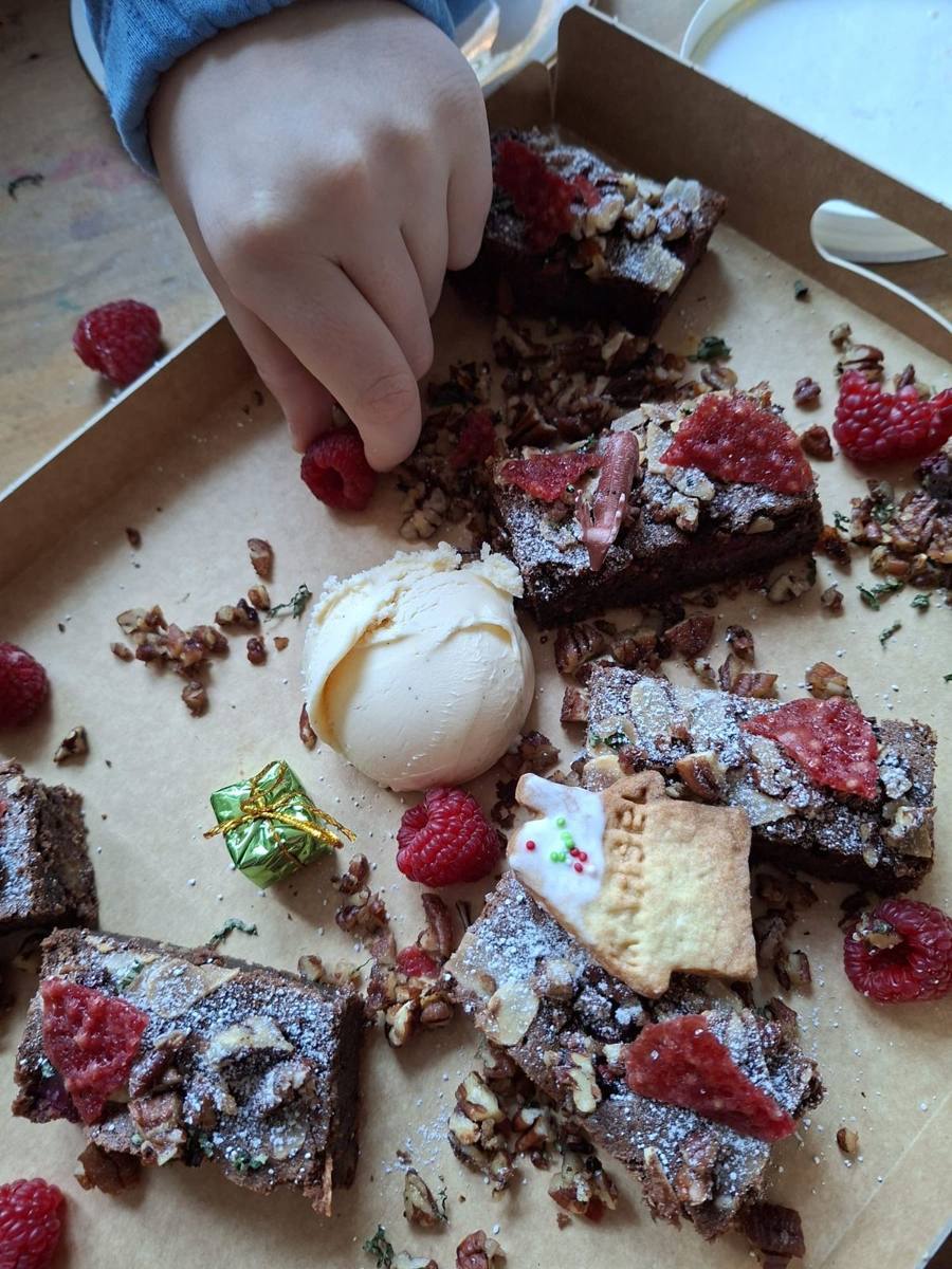 Een kinderhand pakt een framboos tussen brownies en vanille-ijs