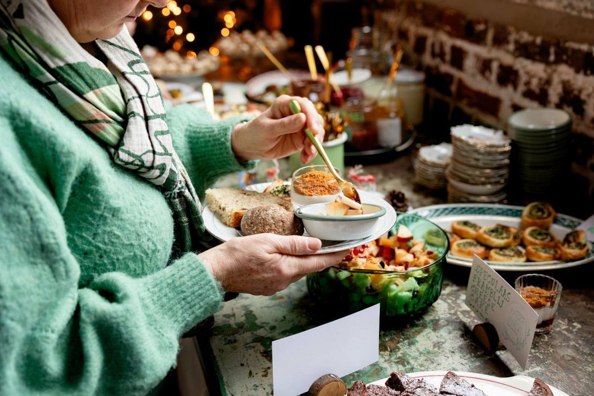 Een gast schept fruitsalade op aan het buffet, met kerstlichtjes op de achtergrond