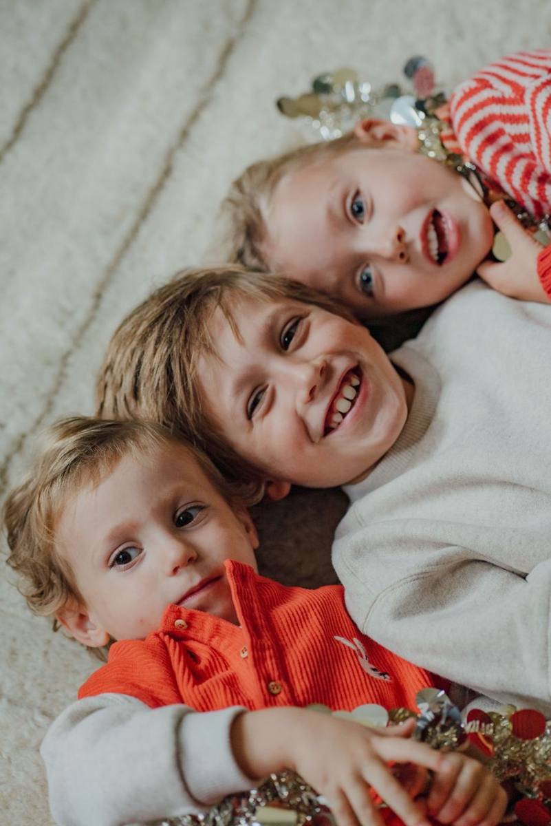 Drie kinderen liggen lachend naast elkaar op een tapijt
